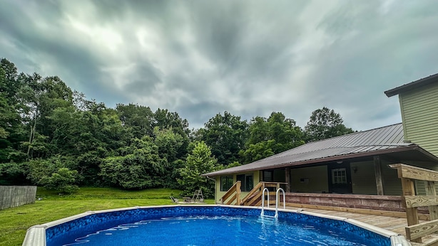 A swimming pool with a wooden deck and a covered area with a metal roof.
