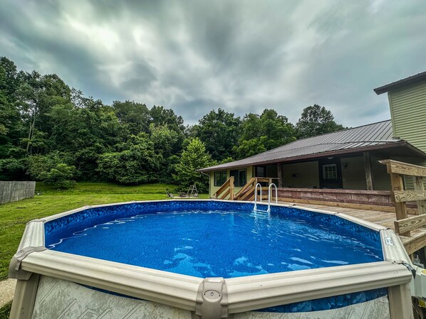 Une piscine dotée d’une terrasse en bois et d’un espace abrité avec un toit en métal.