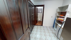 A narrow hallway with wooden doors, a tiled floor, and a laundry area with shelves and a washing machine.