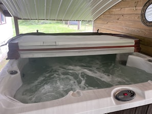 A hot tub with a control panel, wooden walls, and a view of the outdoors.