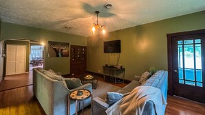 A living room with a sofa, a coffee table, and a TV. There is a door leading to another room and a window with a view.