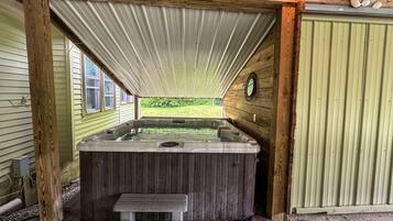 Un espace dédié à un bain à remous, doté d’une terrasse en bois, d’un toit en métal et offrant une vue sur un paysage verdoyant.