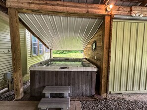 Área de hidromassagem com deck de madeira, cobertura metálica e vista para uma paisagem verde.