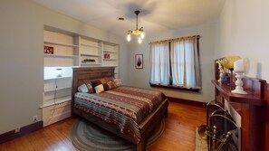 Ein Schlafzimmer mit einem hölzernen Bett, integrierten Regalen, einem Fenster mit Vorhängen und einer Kandelaberleuchte.