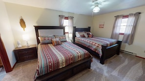 A bedroom with two beds, a nightstand, a lamp, and a ceiling fan.