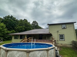 A residential property with a swimming pool, a covered patio, and a house with a metal roof.