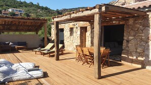 Une terrasse en bois avec des chaises longues, une table et une structure murale en pierre.