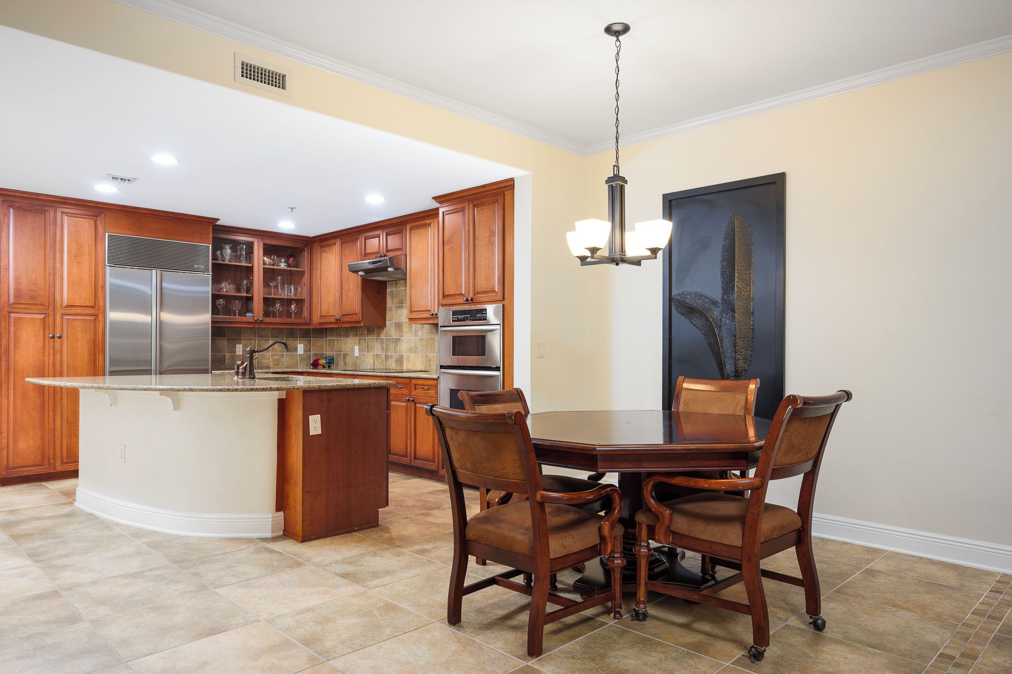 Una cocina con gabinetes de madera, un refrigerador de acero inoxidable, un horno empotrado y una mesa de comedor con sillas.