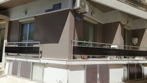 A building with a balcony, a window with a curtain, and a sign with text. - Enjoy Chania (Chania)