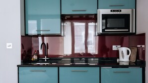 A kitchen with teal cabinets, a black countertop, a microwave, and a kettle.