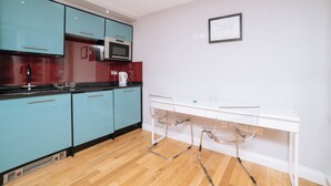 A modern kitchen with teal cabinets, a white countertop, and a glass bar stool.