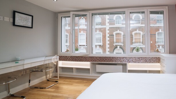 A modern bedroom with a large window, a bedside table, and a bed.