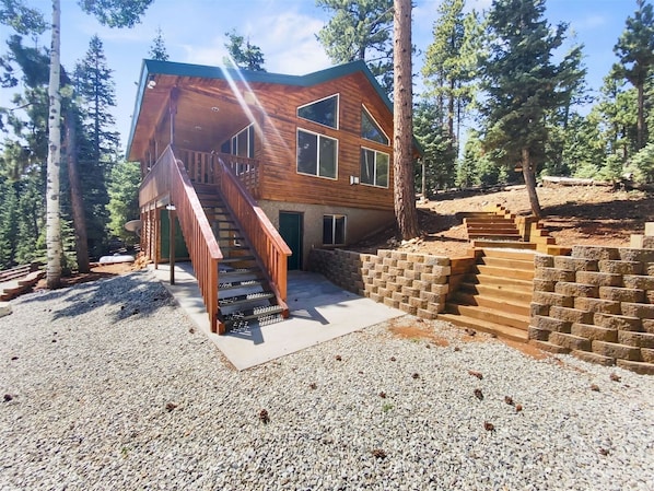 Une cabane avec une façade en bois, un escalier menant à une terrasse et une allée gravillonnée.