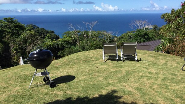 A grassy outdoor area with a barbecue grill and two chairs facing a scenic view of the ocean.