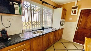 A kitchen with wooden cabinets, a black countertop, a window with bars, a white refrigerator, and a tiled floor.