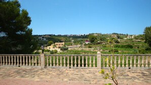 Une terrasse dotée d’un sol carrelé, d’une balustrade et offrant une vue sur une colline, avec des bâtiments et de la végétation.