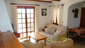 Un salon chaleureux avec un canapé, deux fauteuils en osier, une table en bois et une table à manger avec des chaises.