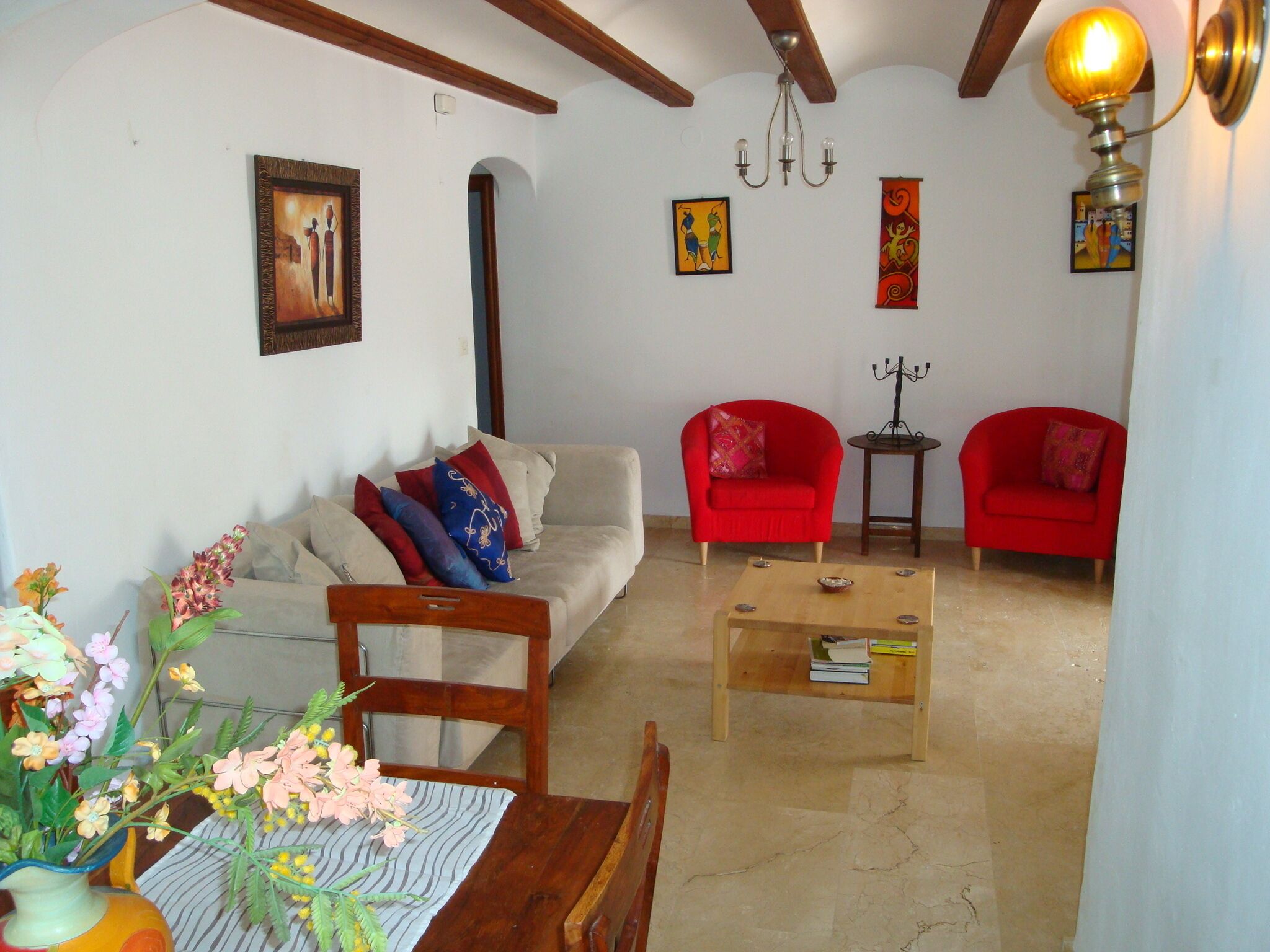Una sala de estar con un sofá, dos sillones rojos, una mesa de centro y una araña.