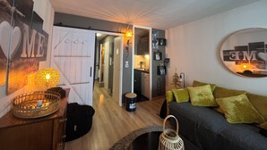 A cozy living room with a sofa, a coffee table, and a decorative lamp. There is a door leading to a kitchen and a hallway.