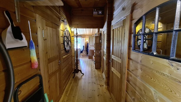 A narrow wooden hallway with a wooden floor, a black and white cat, a colorful mop, and a vintage-style lamp. - Holiday home Kappeled (Smålandsstenar)