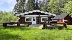 A wooden cabin with a deck, surrounded by lush greenery and trees. - Holiday home Kappeled (Smålandsstenar)