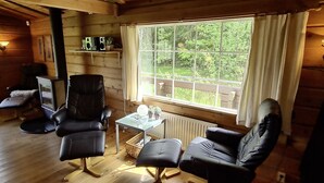 A cozy cabin interior with a large window, wooden walls, a black leather sofa, a glass coffee table, and a television. - Holiday home Kappeled (Smålandsstenar)