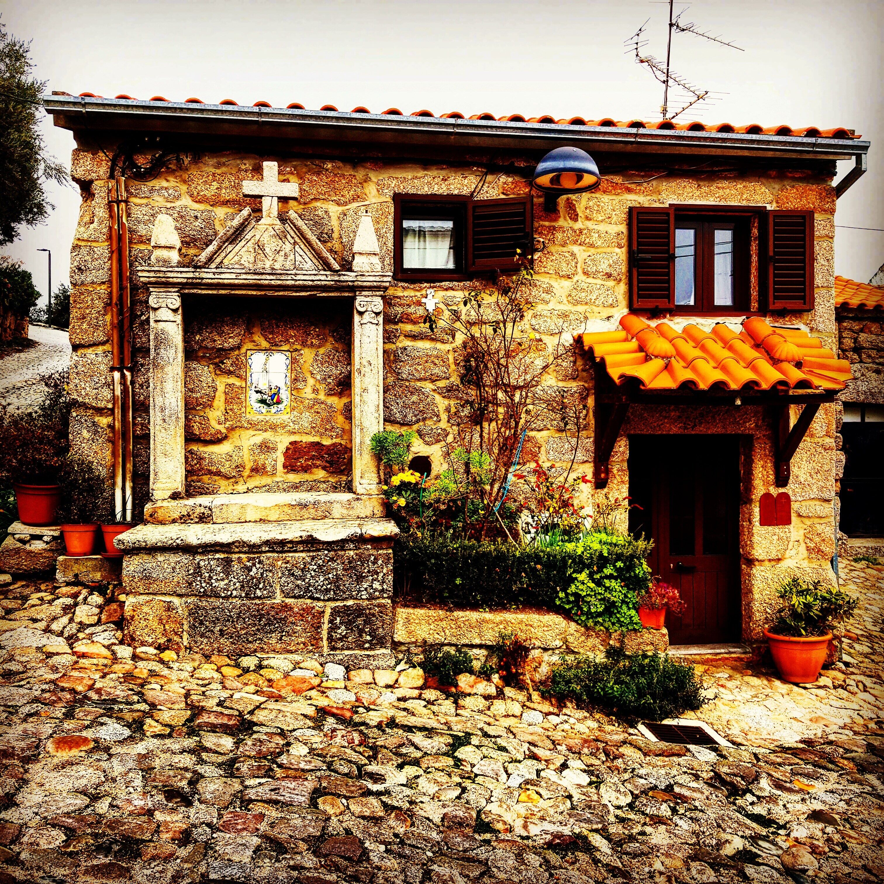 A stone building with a cross, a bell, and a small chapel-like structure.