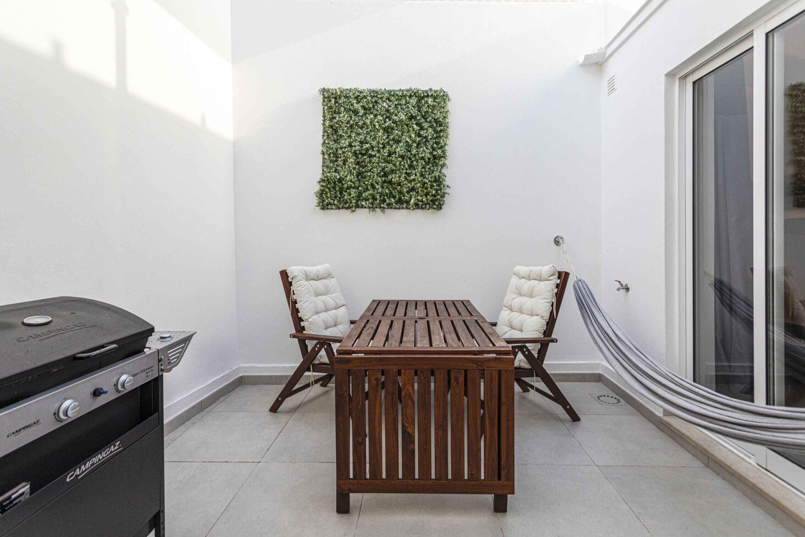 Eine Terrasse mit Holztisch und -stühlen, einem Grill und einer grünen Wanddekoration.