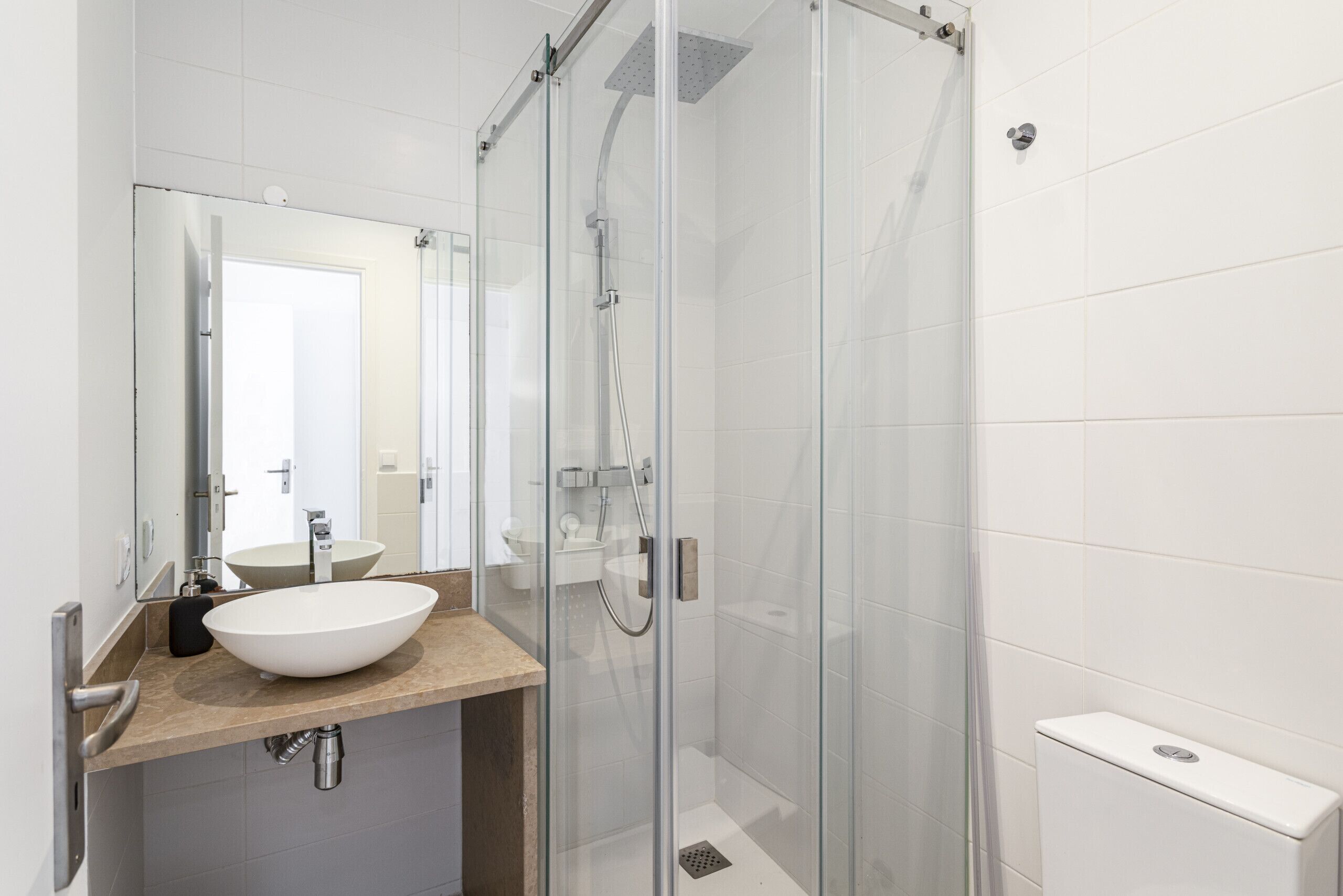 Un baño moderno con ducha de vidrio, lavamanos blanco y un espejo grande.