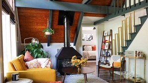 Una sala de estar con chimenea, un sofá amarillo, una mesa redonda con un florero y una escalera.