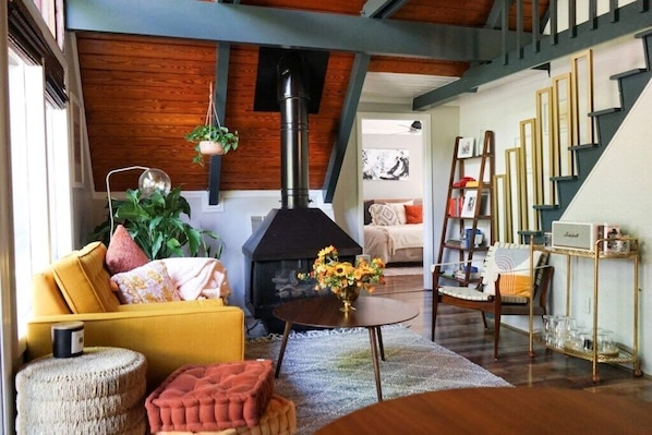 A living room with a fireplace, a yellow sofa, a round table with a vase of flowers, and a staircase.