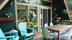 Un patio techado al aire libre con una mesa y sillas de madera, plantas en macetas y vistas al follaje circundante.