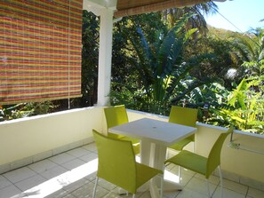 Een terras met een tafel en stoelen, omringd door weelderige begroeiing.