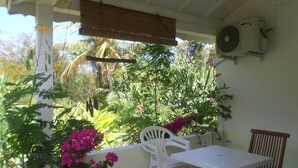 Um pátio externo com mesa e cadeiras, cercado por vegetação exuberante e plantas floridas.