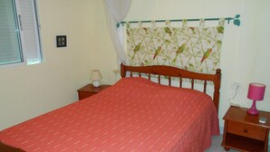 Quarto com cama, mesa de cabeceira, luminária e cortina com padrão de pássaros.