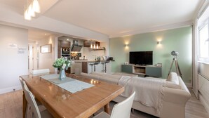 A modern living room with a wooden dining table, a sofa, a TV, and a kitchen in the background. - Stunning Clifton Flat in Amazing Central Location (Bristol)