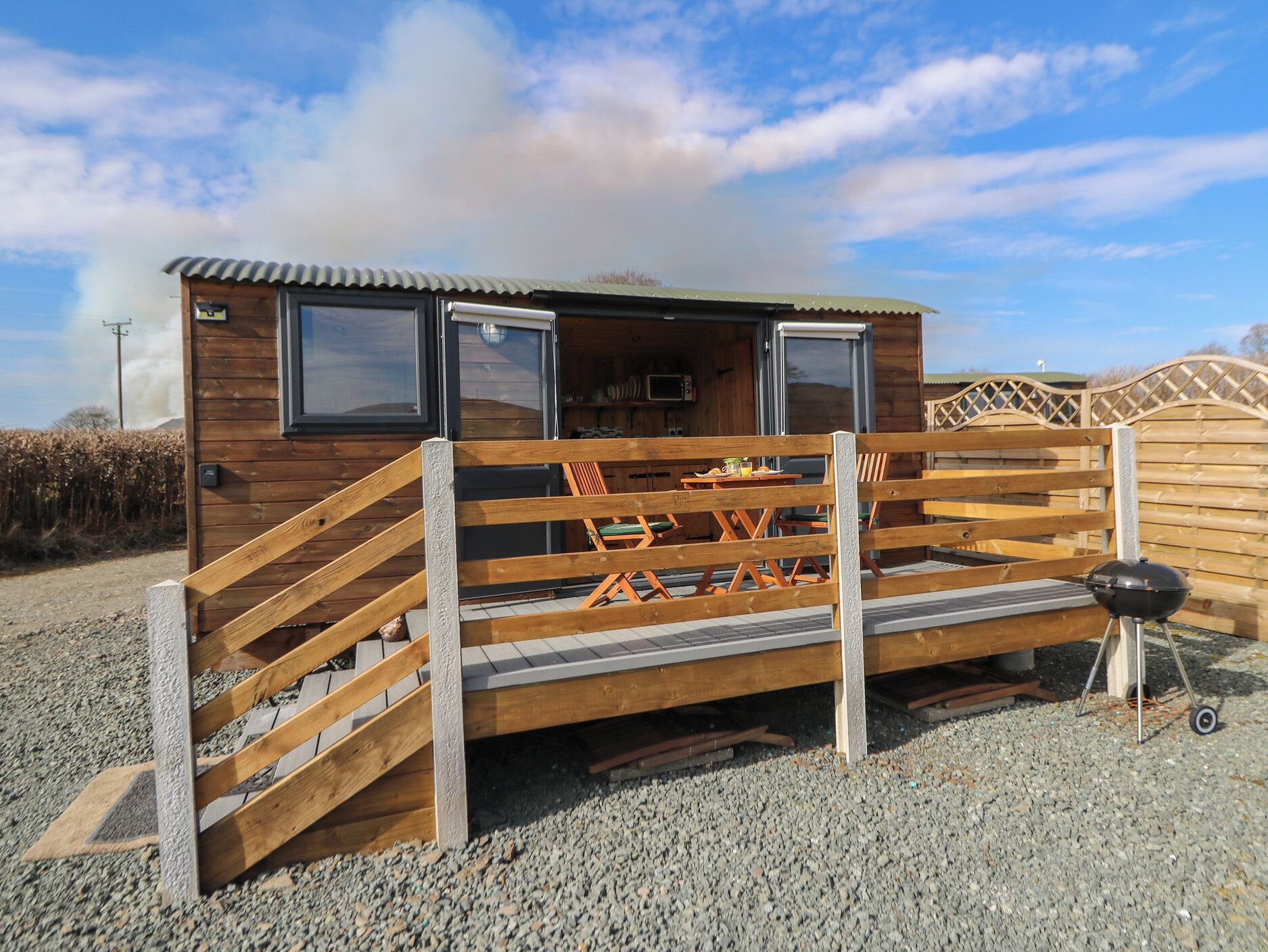 Eine Holzblockhütte mit einer Rampe zu einer Terrasse, einem Grill und einer kleinen Küchenzeile inklusive Mikrowelle.