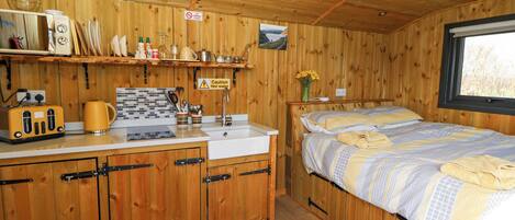 A cabin interior with wooden walls, a kitchenette, a bed with a window, and a bathroom.