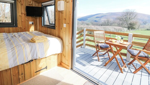 Un dormitorio de cabaña de madera con una cama, un televisor y un amplio ventanal con vistas a un paisaje pintoresco.