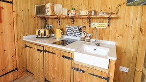 Una cocina de madera pequeña y funcional, equipada con microondas, tostadora, fregadero y diferentes utensilios.