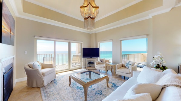 A spacious living room with a television, comfortable seating, a glass coffee table, and large windows offering ocean views.