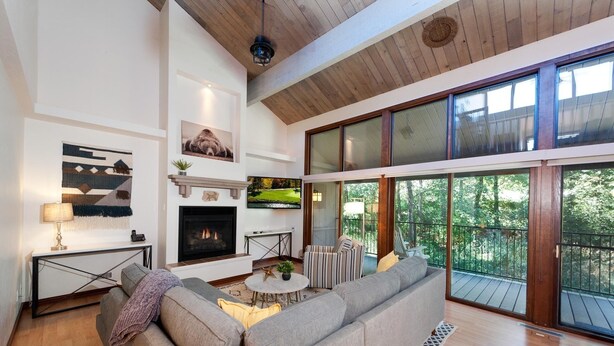 A modern living room with a fireplace, a large sofa, and a view of the outdoors through large windows. - Honey Bear Den | AC, Pool, Hot Tub, Golf & Ski (Durango)