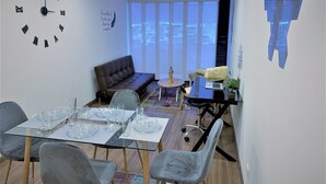 Uma sala de estar moderna com uma mesa de jantar de vidro, cadeiras cinzas, um sofá marrom e um relógio de parede grande.