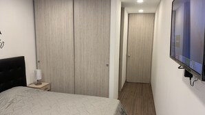 Quarto com cama, mesa de cabeceira, televisão montada na parede e guarda-roupa.