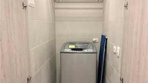 Uma lavanderia compacta com máquina de lavar, um varal e uma toalha azul encostada na parede.