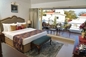A hotel room with a large bed, a balcony with chairs, and a view of buildings. - Casa Ahaana Resort Vagator, by Lavin Hotels (Vagator)