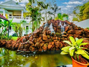 A rock waterfall feature in a garden with a white building in the background. - Casa Ahaana Resort Vagator, by Lavin Hotels (Vagator)
