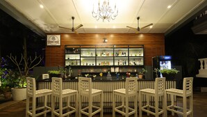 A bar area with white chairs, a wooden bar counter, shelves with bottles, and a Pepsi refrigerator. - Casa Ahaana Resort Vagator, by Lavin Hotels (Vagator)