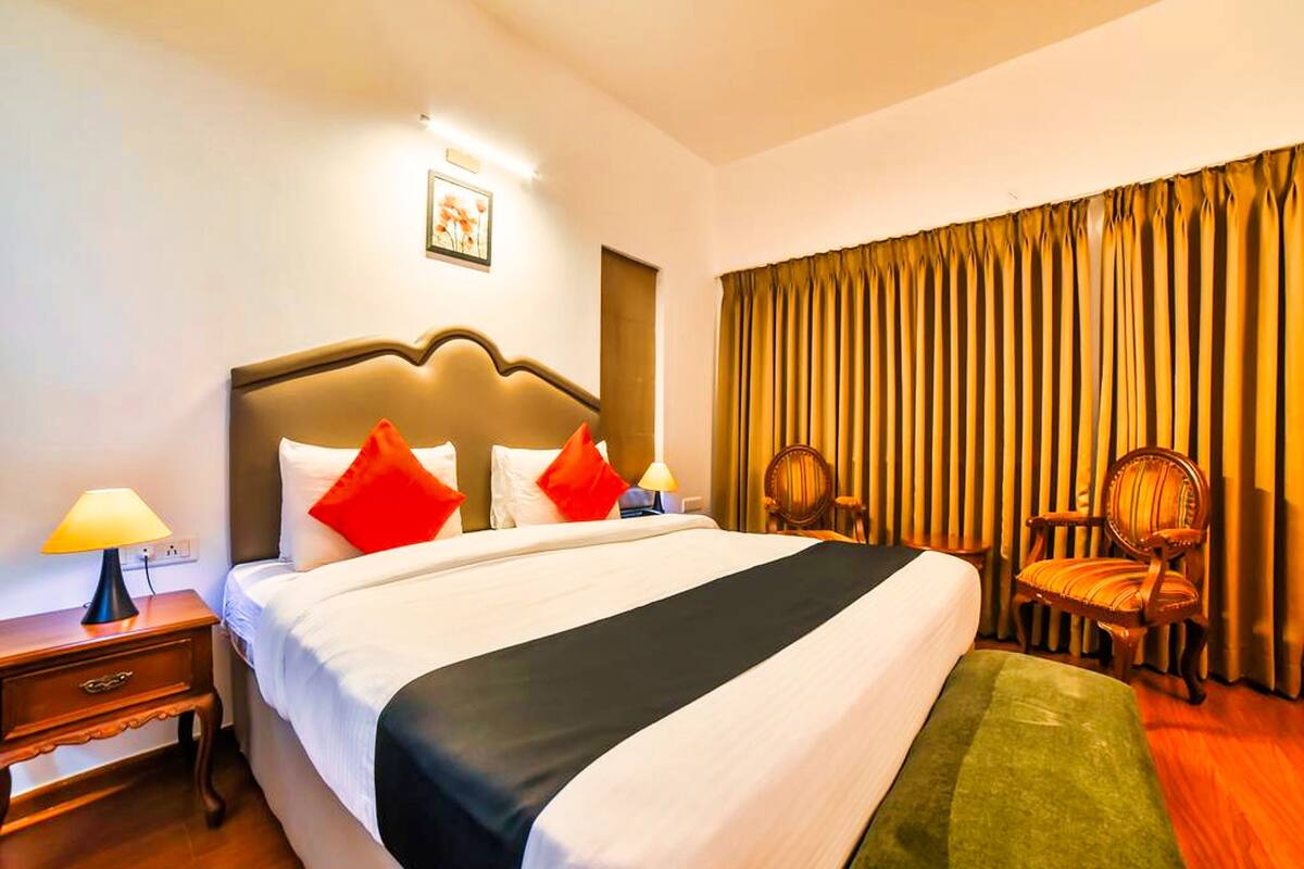 A hotel room with a large bed, two nightstands, a lamp, a chair, and a window with curtains.