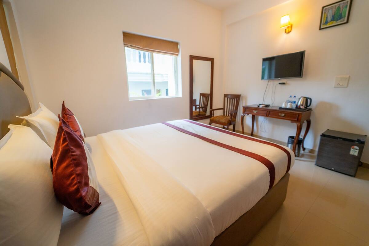 A hotel room with a large bed, a desk with a chair, a television, and a window.